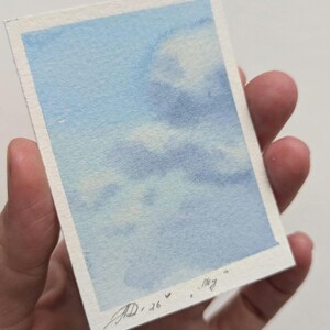 Pu&ograve; includere: Un piccolo acquerello di un cielo blu con nuvole bianche. L'opera d'arte &egrave; firmata e datata "AD, 26" con la parola "Sky" scritta accanto. Il dipinto &egrave; tenuto in una mano.