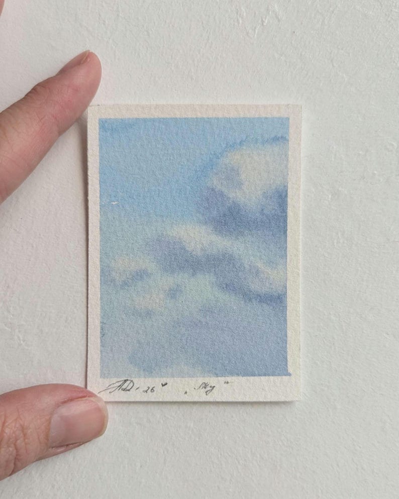 Pu&ograve; includere: Un piccolo acquerello di un cielo blu con nuvole bianche. L'opera d'arte &egrave; su un pezzo di carta rettangolare con un bordo bianco. La firma dell'artista e la parola "Sky" sono visibili nell'angolo in basso a destra.