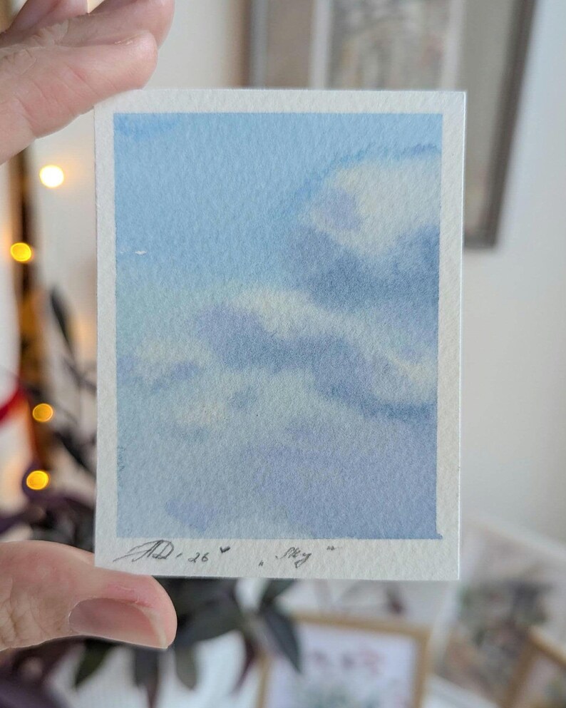Pu&ograve; includere: Un piccolo acquerello di un cielo blu con soffici nuvole bianche. L'opera d'arte &egrave; firmata "AD.26" e include la parola "Sky". Il dipinto &egrave; su un foglio di carta rettangolare con un bordo bianco.