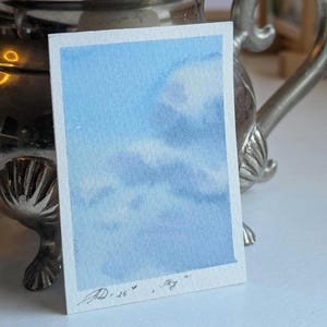 Pu&ograve; includere: Un piccolo acquerello di un cielo blu con soffici nuvole bianche. L'opera d'arte &egrave; firmata e datata "JD '26" con la parola "Sky" scritta sotto. Il dipinto &egrave; su una carta rettangolare bianca.