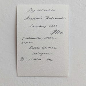 Pu&ograve; includere: Un appunto scritto a mano su carta ruvida. Il testo recita: "Sky collection, Anastasia Rubanonks, January 2026, Watercolor, cotton paper, Odosa, Ukraine, instagram @nastasia-sea."