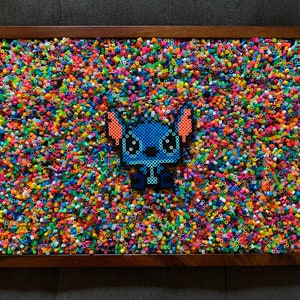 May include: A blue and orange Stitch character made from colorful plastic beads, set against a background of multi-colored beads.