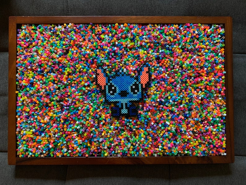 May include: A blue and orange Stitch character made from colorful plastic beads, set against a background of multi-colored beads.