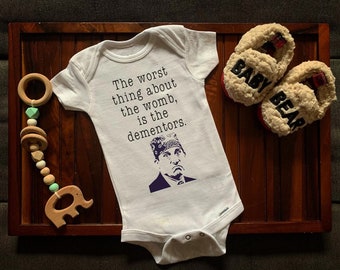 Puede incluir: Un body blanco para bebé con una imagen en blanco y negro de un personaje de la serie de televisión "The Office" y el texto "The worst thing about the womb, is the dementors."