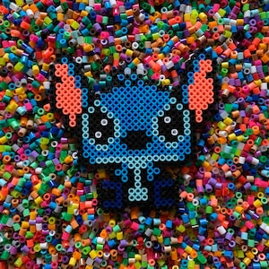 May include: A blue, orange, and black pixel art character resembling Stitch from Lilo & Stitch, surrounded by colorful plastic beads.