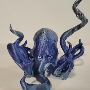 May include: A blue 3D printed octopus figurine with large eyes. The octopus has eight tentacles and is posed in a curled position.