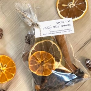 May include: A clear plastic bag filled with dried orange slices, cinnamon sticks, and other spices. The bag is tied with twine and has a white tag that reads "Stove Top Holiday Blend Simmers" and instructions for use.