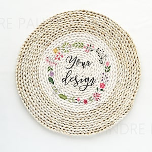May include: Round woven placemat with a floral wreath design and the words "Your design" in black script. The placemat is made of natural-colored woven material, and the floral wreath features pink, yellow, and purple flowers.