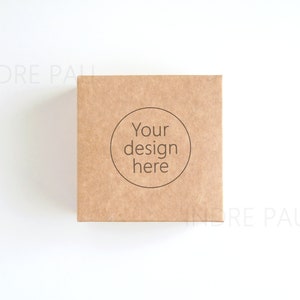 May include: A square, brown cardboard box with the text "Your design here" inside a circle. The box is centered on a white background, with the brand name "INDRE PAU" faintly visible in the corners.