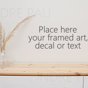 May include: A clear glass vase with dried wheat stalks sits on a light wood surface. The text "Place here your framed art, decal or text" is displayed on the off-white wall behind the vase and table.