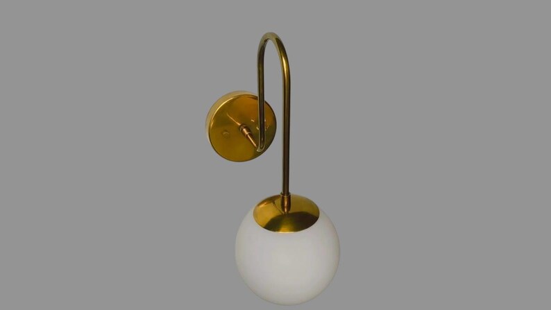 May include: A contemporary wall light with a gold finish and a white globe shade. The sconce features a circular wall mount, a curved arm, and a spherical light fixture. The design is minimalist and elegant, suitable for various interior styles.