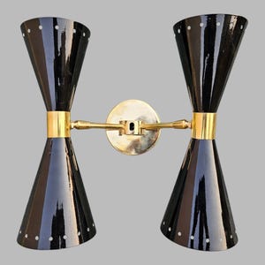 Peut inclure: Une paire d'appliques murales noires et dorées au design moderne. Chaque applique possède deux abat-jours coniques noirs avec des accents dorés.