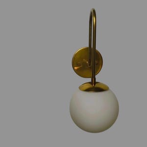 May include: A wall-mounted light fitting with a brass finish and a white, spherical glass shade. The fitting has a circular base and a curved arm supporting the globe. The design is simple and elegant, suitable for various interiors.