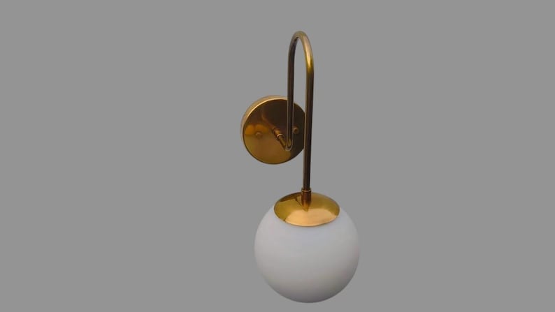 May include: A contemporary wall light with a white globe shade and a curved, brass-coloured arm. The light has a circular base and a matching brass-coloured cap. The fixture is designed for wall mounting and provides ambient lighting.