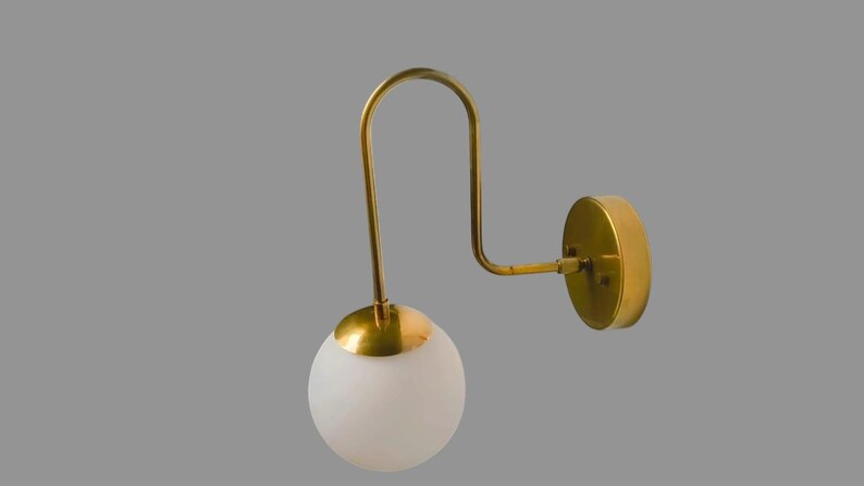 May include: A contemporary wall light featuring a gold-toned metal frame and a spherical, frosted glass shade. The fixture has a curved arm and a circular wall plate. The design is minimalist and suitable for various interior styles.