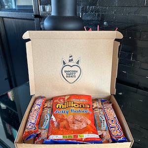 May include: A brown cardboard box with a unicorn logo that says "Unicorn Sweet Boxes". The box is open and contains three bags of sweets: a bag of orange "Millions Jelly Babies", a bag of orange "Millions" chocolate bars, and a bag of orange "Millions" chocolate bars.