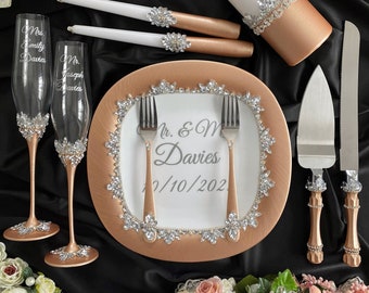 May include: Rose gold wedding cake serving set with a white cake knife, two champagne flutes, two candles, and a cake plate with the text "Mr. & Mrs. Davies 12/10/202".
