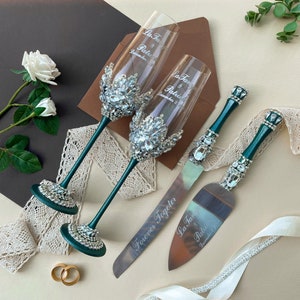 May include: A wedding cake cutting set with two emerald green champagne flutes and a knife. The flutes are decorated with rhinestones and have the names "La Tan & Patrick" and the date "December 2" engraved on them. The knife has the words "Forever Together" and "La Tan & Patrick" engraved on it.