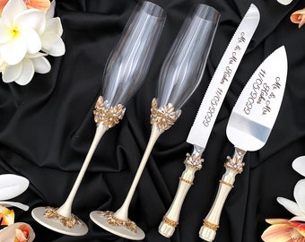 May include: A wedding cake cutting set with two champagne flutes and a cake knife. The flutes and knife handles are decorated with gold and white embellishments. The knife is engraved with "Mr. & Mrs.  Hayden 11/11/2023" and the server is engraved with "Mr. & Mrs. Hayden 11/11/2023".