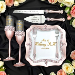 May include: A pink and silver cake knife and server set with a pink and white plate decorated with rhinestones. The plate features the text "Mis 15 Hillary R.H 10-09-2006" in gold lettering. Two pink champagne flutes with rhinestones are also included.