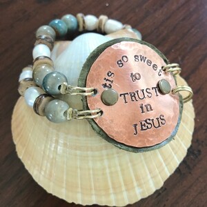 May include: A copper charm bracelet with a green leather backing and the words "'tis so sweet to TRUST in JESUS". The bracelet is made with brown and white beads and blue and green stones.