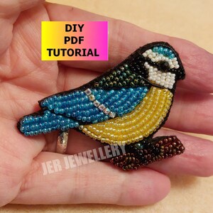 May include: A beaded bluebird brooch with a yellow breast, black head, and brown legs. The brooch is on a hand and has a DIY PDF tutorial label.