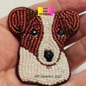 May include: A beaded dog head brooch with brown and white beads. The dog has black eyes and a pink nose. The brooch is labeled "JER Jewellery 2022".