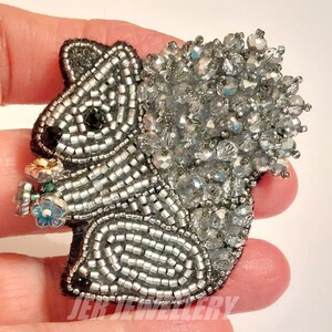 May include: A silver beaded squirrel brooch with a crystal-like tail and a small bouquet of flowers in its mouth.