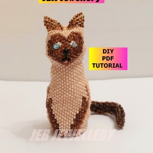May include: A beaded Siamese cat figurine made with brown and light pink beads. The cat is sitting with its tail curled around its body. The image includes the text "JER Jewellery" and "DIY PDF TUTORIAL".