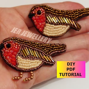 May include: Two beaded robin bird brooches with red, brown, and white beads. The brooches are on a hand and have a DIY PDF Tutorial label.