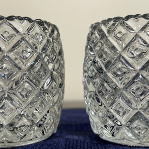 May include: Two clear glass candle holders with a diamond pattern. The holders are cylindrical and have a slightly flared top.