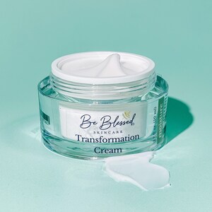 Puede incluir: Un tarro transparente de crema blanca con tapa blanca. El tarro está etiquetado con "Be Blessed Skincare Transformation Cream" y "1.7 fl oz (50 ml) Moisture".