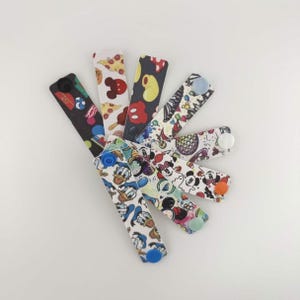 May include: A selection of patterned button extenders. Designs include Mickey Mouse, Donald Duck, pizza slices, and abstract patterns. Each extender has a button on one end and a buttonhole on the other.