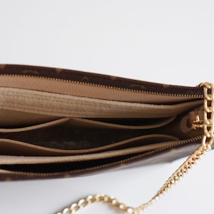 Op de afbeelding: Een bruine en beige monogram tas met een gouden kettingriem. De tas is open en toont drie binnenzakken.