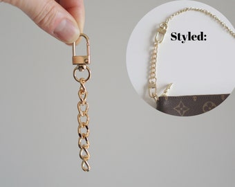 May include: Gold chain with a lobster clasp on one end and a swivel clasp on the other. The chain is styled to be used as a purse strap.