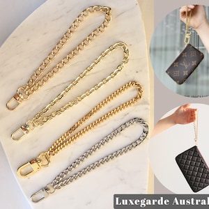 May include: Gold, silver, and gold-tone chain wrist straps with lobster claw clasps. Two purses are shown with wrist straps attached. The purses are brown with a logo and black with a quilted pattern.