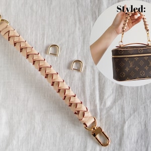 May include: A braided leather strap with gold hardware and two gold D-rings. The strap is beige with a red accent. The text "Styled:" is visible in the background.