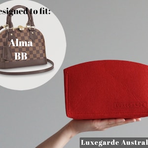 May include: Red felt bag designed to fit a Louis Vuitton Alma BB handbag. The bag has the text "Luxegarde" printed on the front.