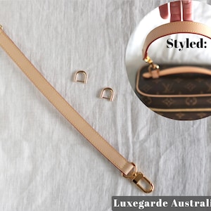 May include: A beige leather strap with gold hardware, two gold D-rings, and a gold swivel hook. The strap is shown on a white fabric surface. The image also shows a close-up of a brown and beige handbag with the text "Styled:" on the image.