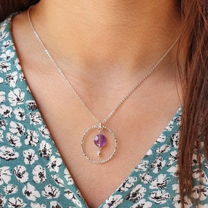 Puede incluir: Un collar de cadena de plata con un colgante circular texturizado con una piedra de amatista p&uacute;rpura.
