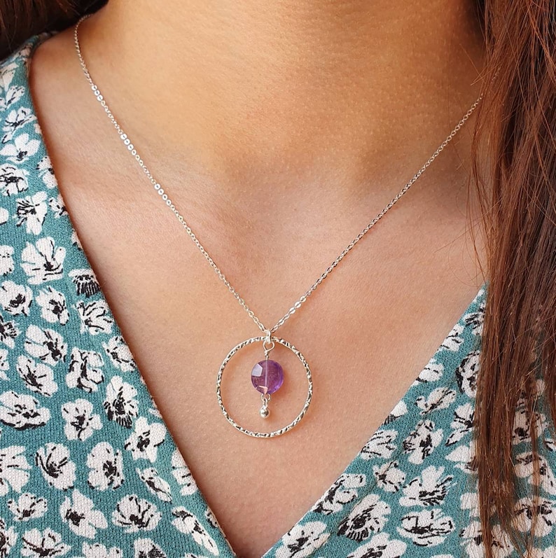 Puede incluir: Un collar de cadena de plata con un colgante circular texturizado con una piedra de amatista p&uacute;rpura.
