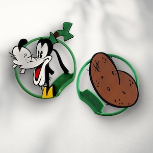 May include: Green plastic cookie cutters shaped like a cartoon dog and a potato. The dog is wearing a green hat and has a brown nose and black eyes. The potato is brown and has a rough texture.