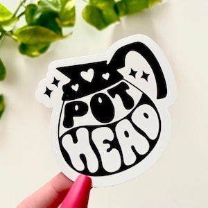 May include: Black and white sticker of a coffee pot with the text "POT HEAD" in a retro font.