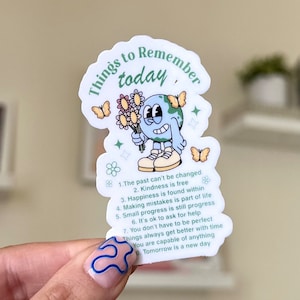 May include: A white sticker with a cartoon illustration of a blue globe holding a bouquet of flowers. The sticker has the text "Things to Remember today" and a list of positive affirmations: "The past can't be changed", "Kindness is free", "Happiness is found within", "Making mistakes is part of life", "Small progress is still progress", "It's ok to ask for help", "You don't have to be perfect", "Things always get better with time", "You are capable of anything", "Tomorrow is a new day".