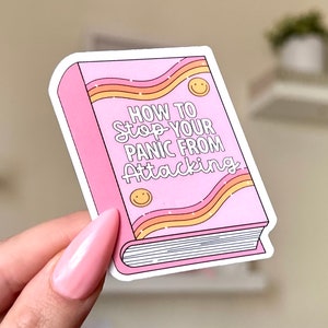 Puede incluir: Pegatina rosa y amarilla con el texto "How to Stop Your Panic From Attacking" en blanco. La pegatina tiene forma de libro con un diseño ondulado.