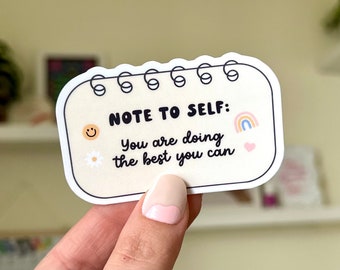 May include: A white sticker with rounded edges that says "Note to self: You are doing the best you can." It has a smiley face, a daisy, a rainbow, and a heart on it.
