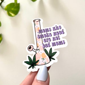 May include: A sticker with a purple and white design of a bong with a lemon pattern and the text "Moms who smoke weed are not bad moms".