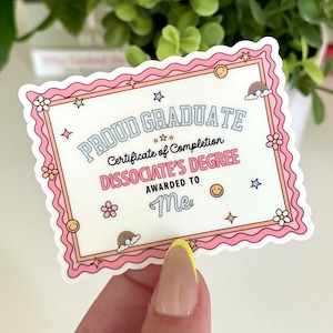 May include: A pink and white certificate with a wavy border. The certificate reads "Proud Graduate Certificate of Completion Dissociate's Degree Awarded to Me".