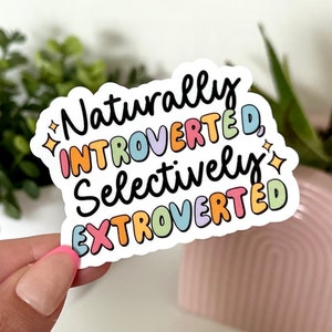 May include: A white sticker with the text "Naturally Introverted, Selectively Extroverted" in colorful letters. The letters are outlined in black and have a rainbow color scheme.