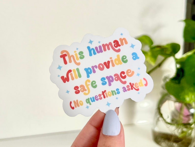 Op de afbeelding: Een regenboogkleurige sticker met de tekst "This human will provide a safe space (no questions asked)".